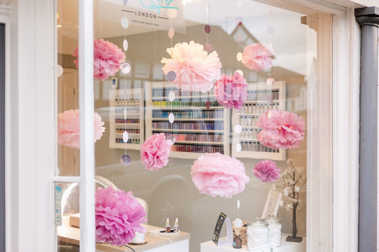 The shop window with pink pom-poms, looking in at the wall of polish