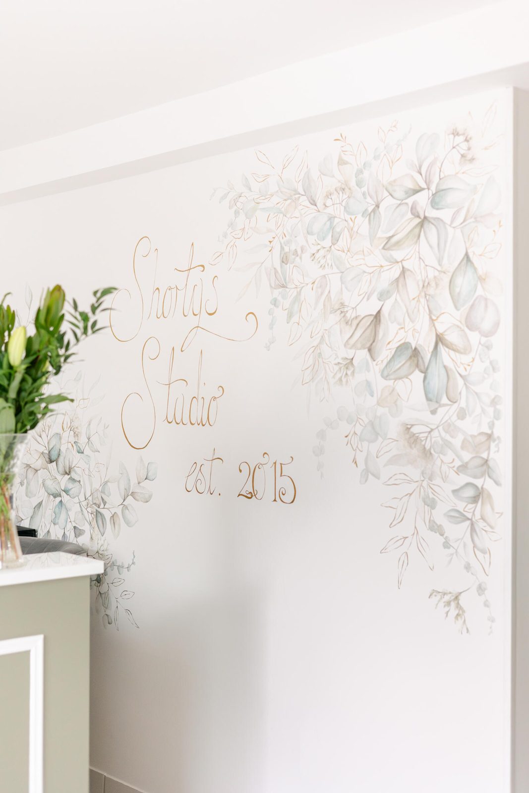 The hand-painted botanical wall at Shorty's Studio, lettered est. 2015 in gold